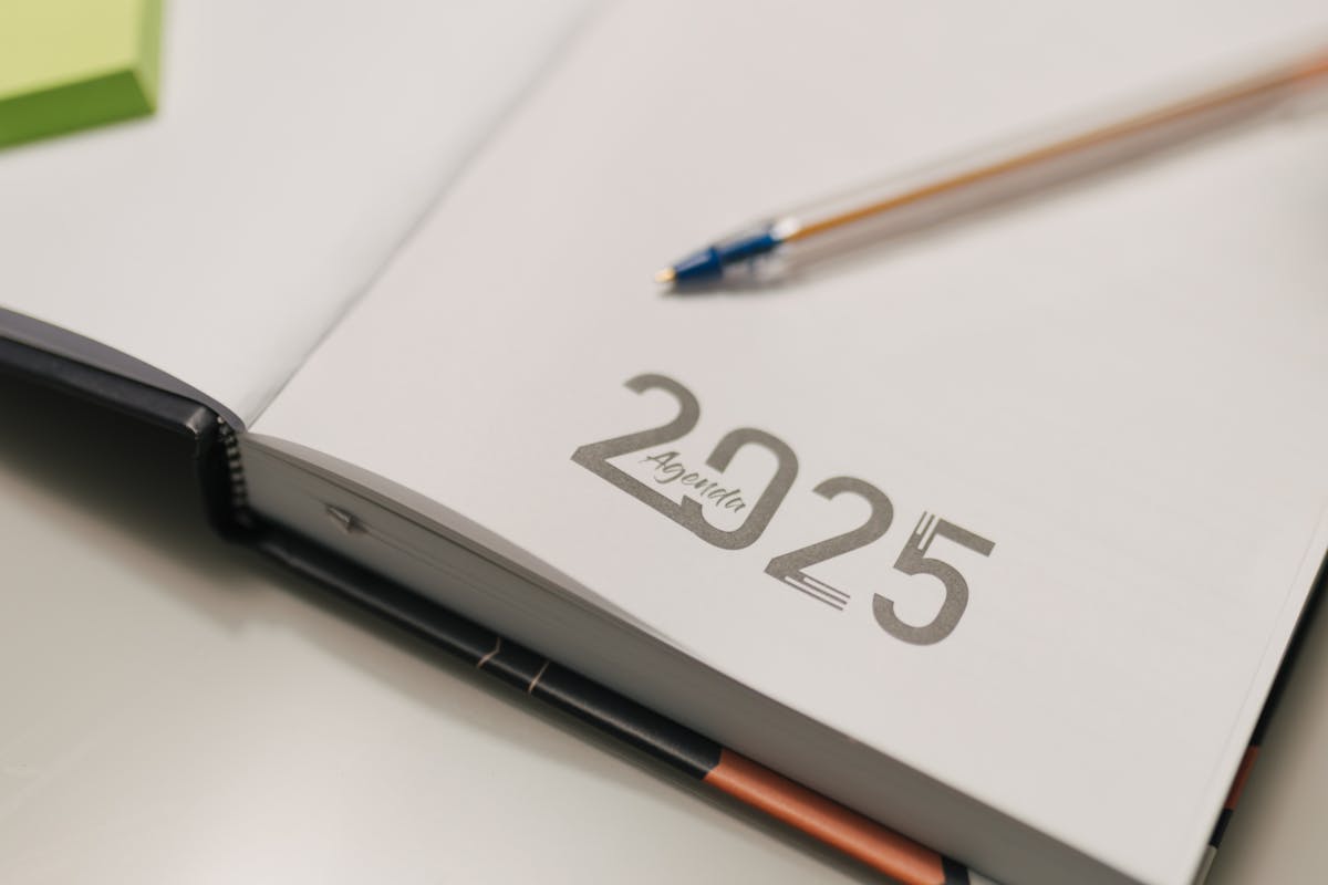 Open 2025 agenda book with a blue pen on a desk, ideal for organization and planning.