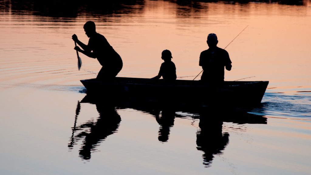 silhouette of three person riding on boat on body of water