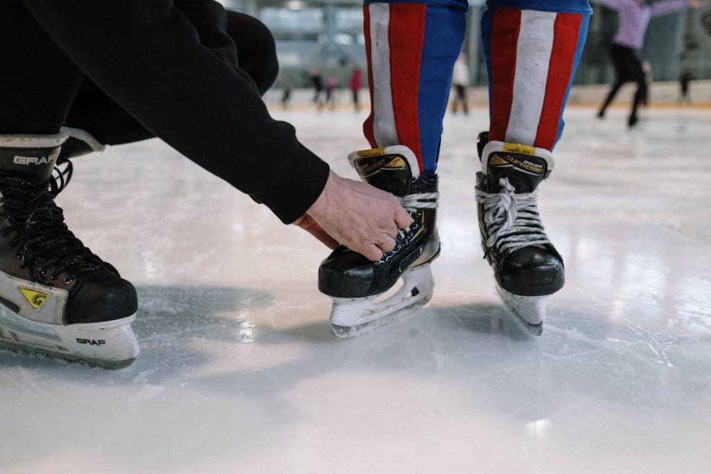 A child getting help tying ice skate laces at a skating rink. Perfect for winter sports themes.