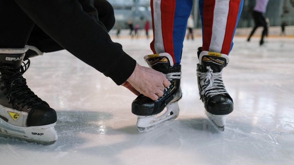 A child getting help tying ice skate laces at a skating rink. Perfect for winter sports themes.