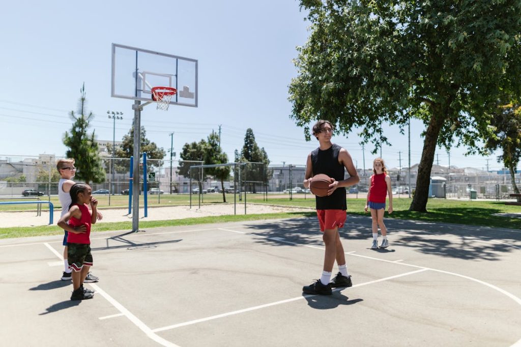 Children and teenagers practicing basketball outdoors on a sunny day.