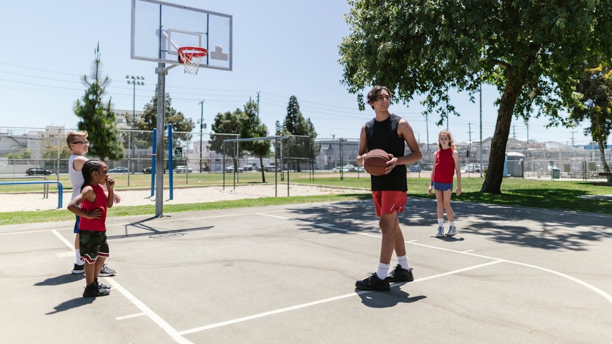 Children and teenagers practicing basketball outdoors on a sunny day.