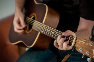 A musician strums chords on an acoustic guitar, showcasing musical talent.